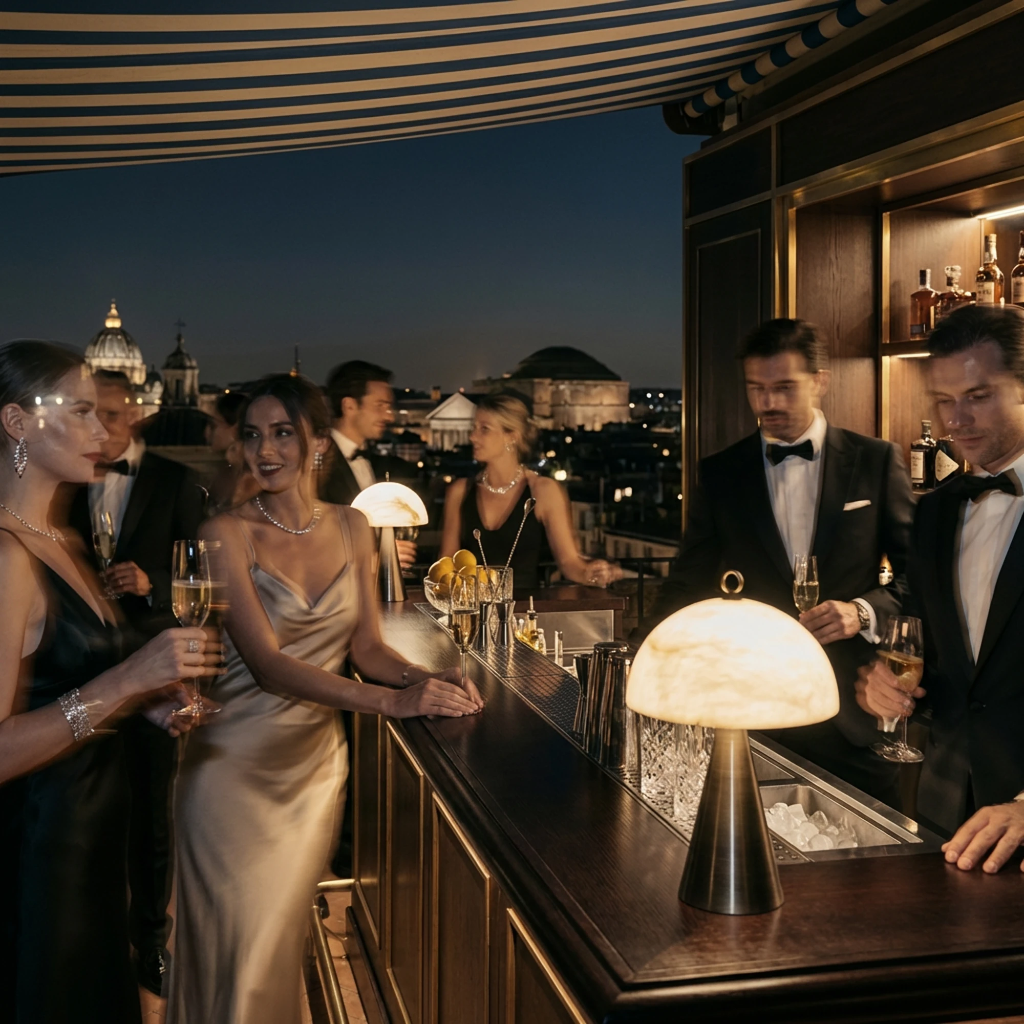 Persone in abito da sera al bar di una terrazza romana, illuminate dalle lampade da tavolo.